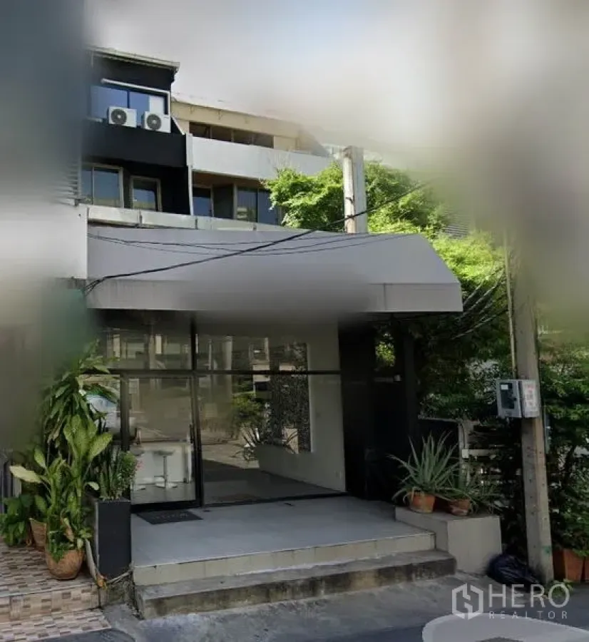 店屋 出租在Watthana, Bangkok - 带玻璃门面与雨棚的商用联排入口，两侧摆放绿植