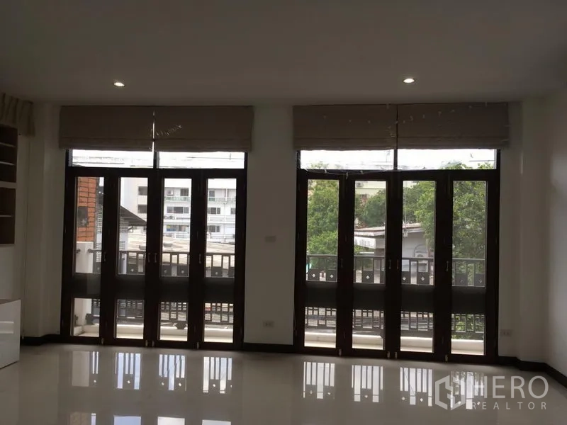 ทาวน์เฮาส์ ให้เช่าในWatthana, Bangkok - ห้องที่มีประตูกระจกฝรั่งเศสสามชุด เปิดสู่ระเบียงยาวและวิวเมืองต้นไม้
