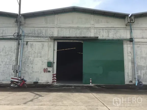 Warehouse for rent in Khlong Luang, Pathum Thani - Industrial warehouse exterior with wide green sliding door and loading access.