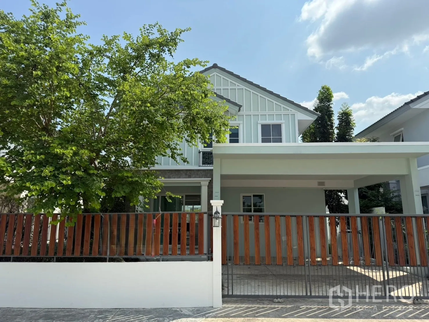 Detached House for rent in Bang Phli, Samut Prakan - Front view of a two-storey detached house with a covered carport, wooden gate, and a large leafy tree.