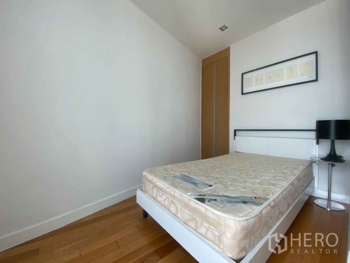 Condominium for rent or sale in Khlong Toei, Bangkok - Second bedroom with minimalist bed, built-in wardrobe and framed artwork.