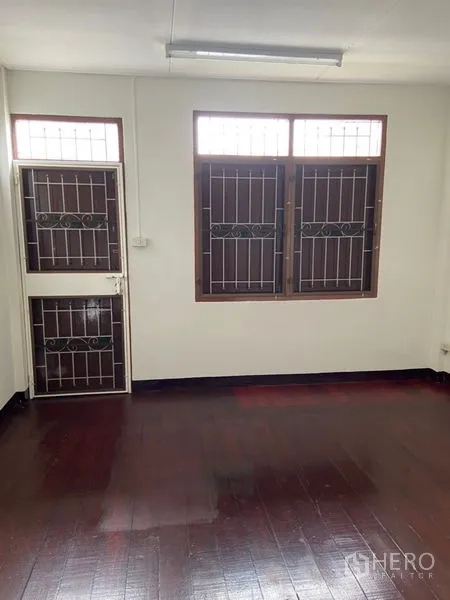 Shophouse for rent in Khlong Toei, Bangkok - Upper-level room with door to a small balcony and twin windows with security bars.