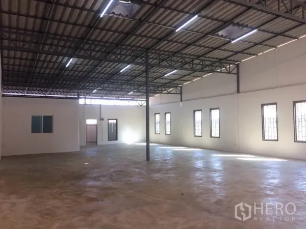 Warehouse for rent in Pathum Thani - Open-plan storage space with bright strip lighting, security-bar windows, and smooth concrete flooring.