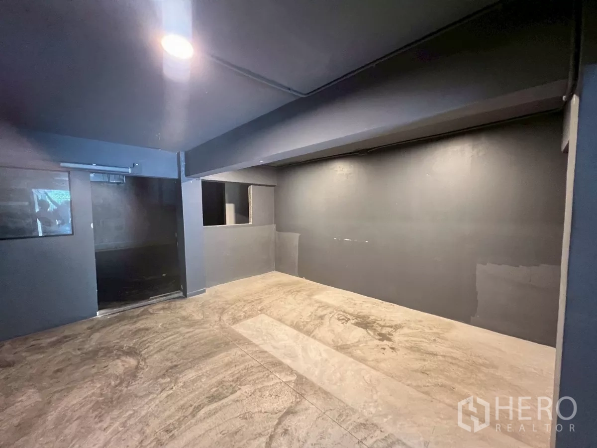 Shophouse for rent in Watthana, Bangkok - Open dark grey room with recessed lighting and a concrete floor.