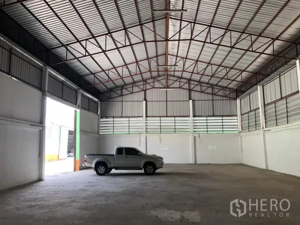 Warehouse for rent in Pathum Thani - Open warehouse floor with high ceiling, vented walls and a pickup truck showing generous loading space.