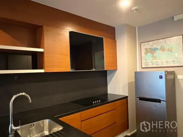 Condominium for rent - Compact kitchen with wood cabinets, black countertop, electric hob and stainless‑steel fridge.