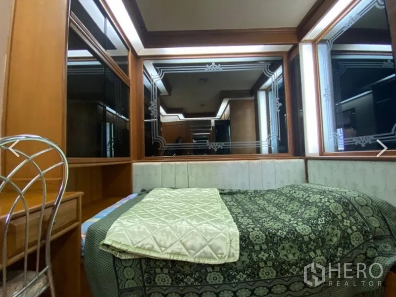 Condominium for sale in Watthana, Bangkok - Cozy bedroom with upholstered headboard, patterned bedding and large decorative mirrored panels.