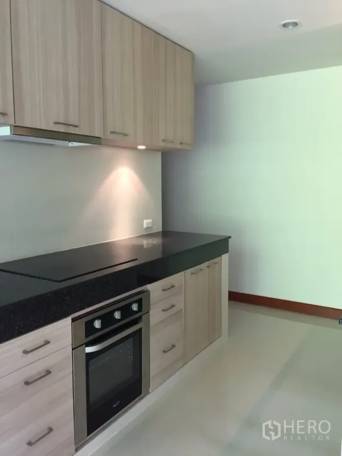 Detached House for rent in Sathon, Bangkok - Modern kitchen with black granite countertop, built-in oven and light wood cabinets.