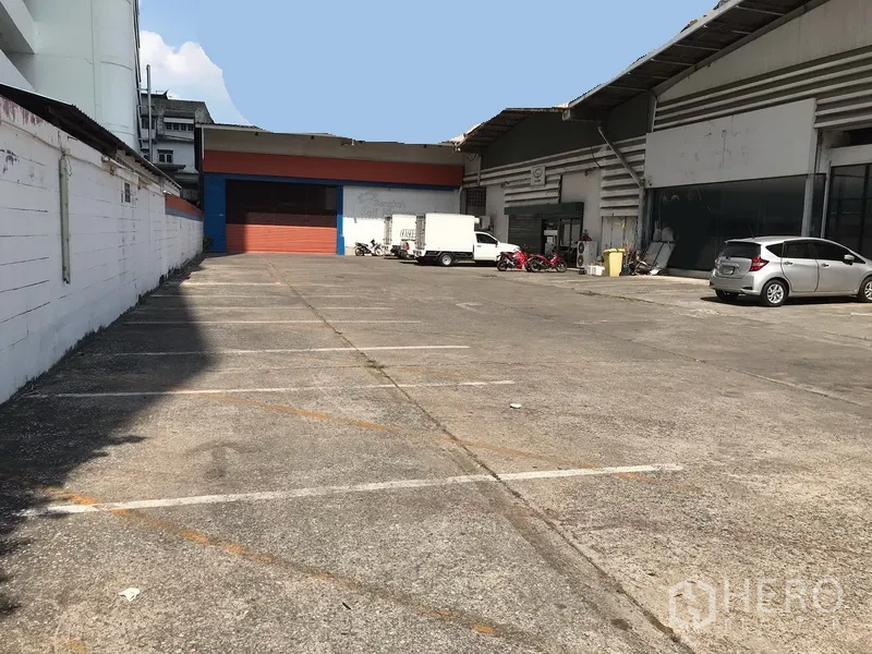 Warehouse for rent in Khlong Toei, Bangkok - Spacious concrete yard with marked parking bays and a loading bay between adjoining warehouse buildings.