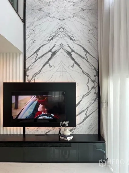 Detached House for rent or sale in Bang Phli, Samut Prakan - Double-height living room TV wall clad in bookmatched marble with a sleek black media console and sheer curtains.