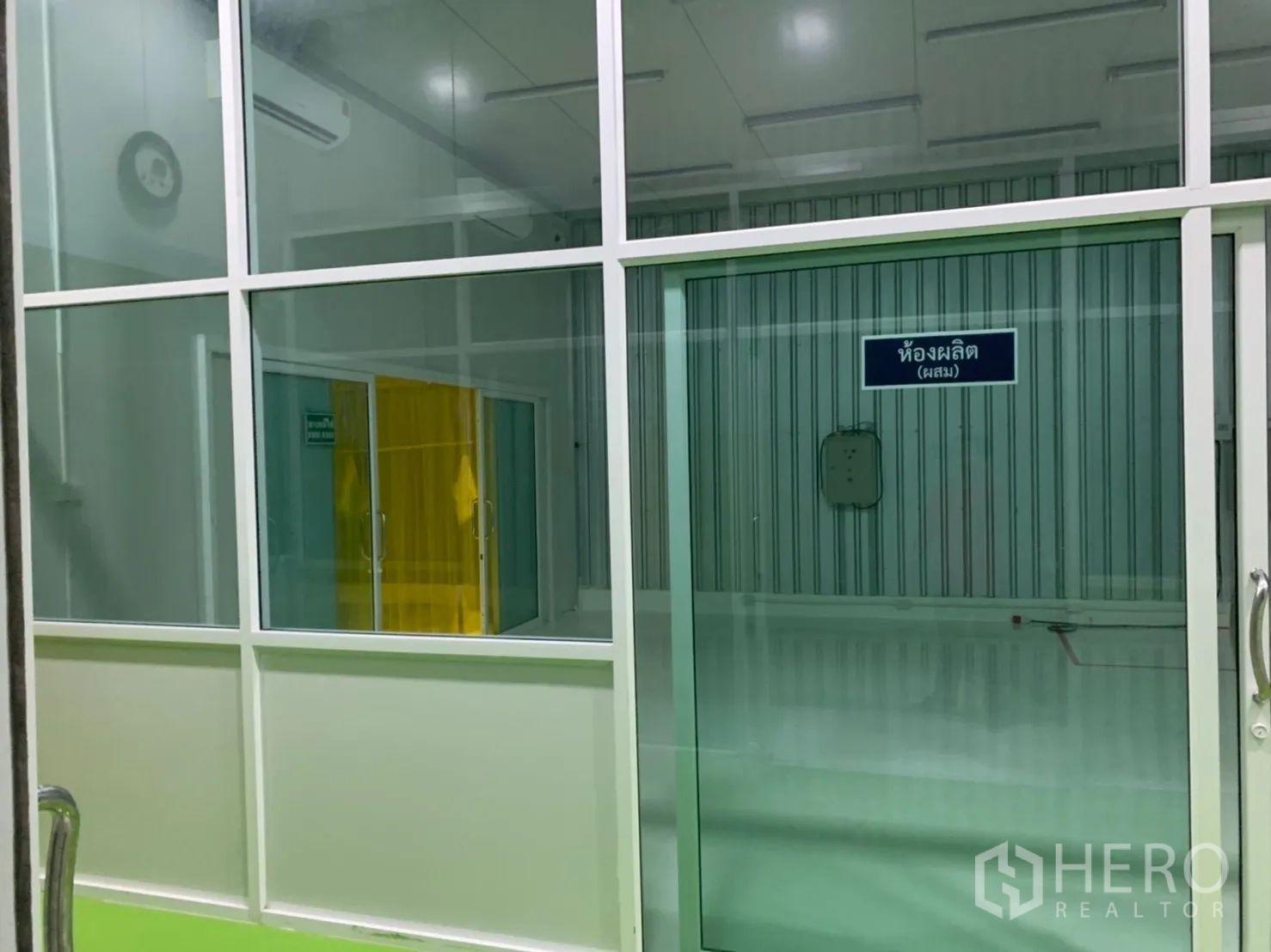 Factory for rent in Khlong Luang, Pathum Thani - Glass-partitioned production room with sliding doors and an air conditioner.