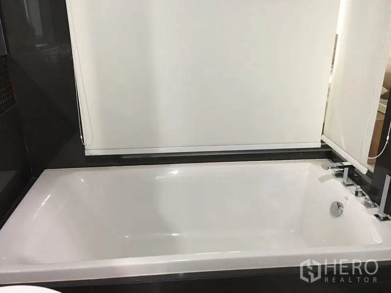 Condominium for rent in Khlong Toei, Bangkok - Clean white bathtub with chrome fixtures in a modern tiled bathroom.