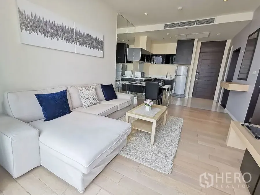 Condominium for rent in Watthana, Bangkok - Light-filled lounge with chaise sofa, textured rug and mirror wall reflecting the kitchen.