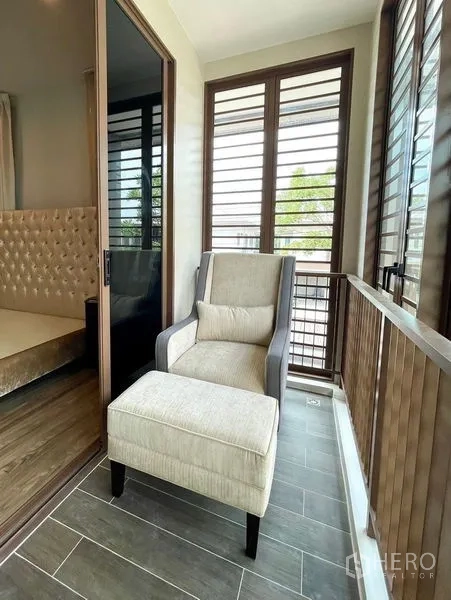 Detached House for sale in Bang Kapi, Bangkok - Covered balcony with louvered screens and a cushioned armchair and ottoman by sliding glass doors.