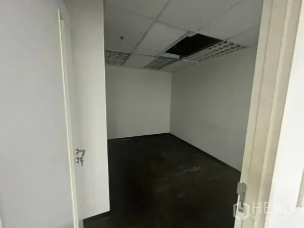 Office Space for rent in Khlong Toei, Bangkok - Small empty office with dark carpet tiles, suspended ceiling lights and an open door.