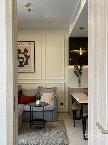 Condominium for rent in Pathum Wan, Bangkok - Cozy living room with L-shaped sofa, wall art and a dining nook beside the pantry.