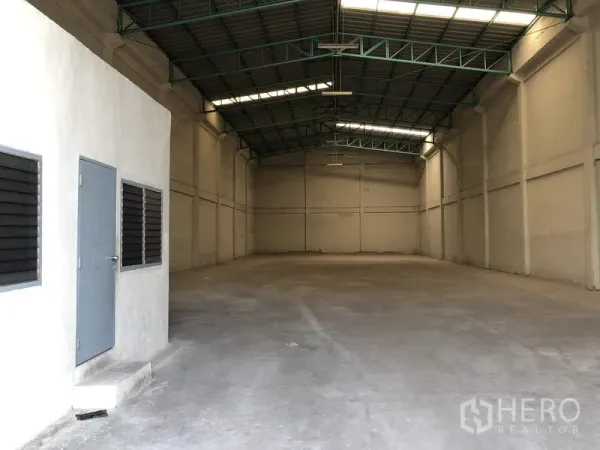 Warehouse for rent in Khlong Luang, Pathum Thani - Spacious clear-span warehouse interior with high steel truss roof and small office block.
