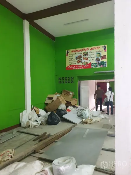 Shophouse for rent in Phra Khanong, Bangkok - Ground‑floor interior under renovation with bright green walls, debris and building materials on the floor.