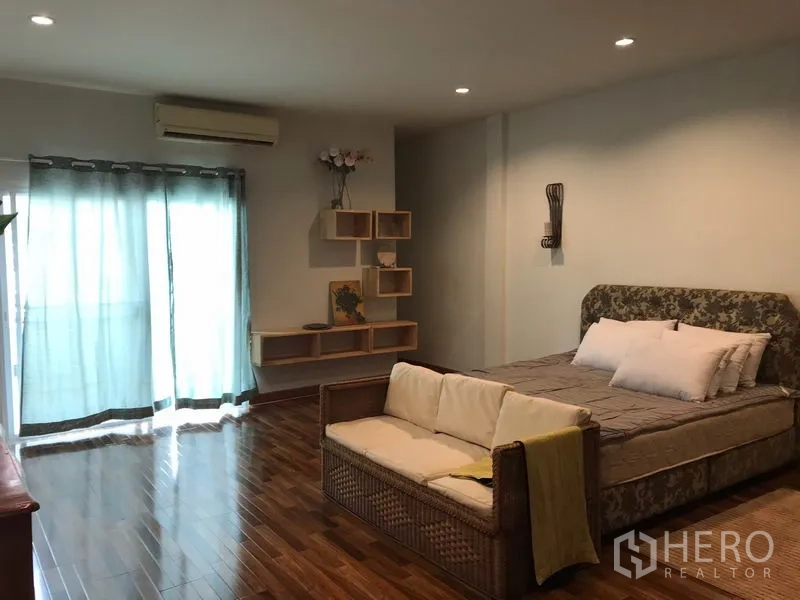 Townhouse for rent or sale in Phra Khanong, Bangkok - Large master bedroom with king bed, sofa seating, air conditioner and display shelves.