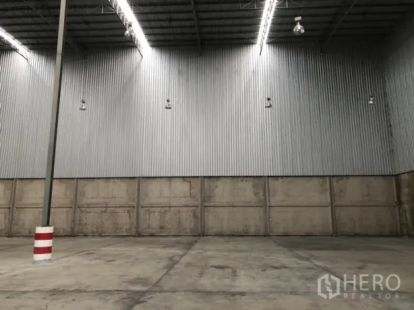 Warehouse for rent in Lam Luk Ka, Pathum Thani - Close-up of corrugated steel wall, high-bay lights and reinforced concrete flooring.