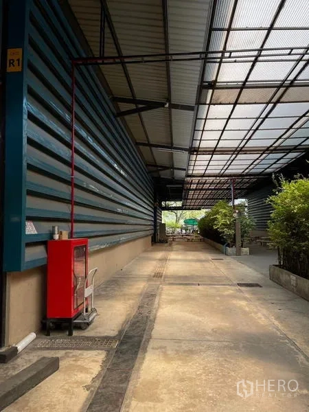 Warehouse for rent in Si Racha, Chon Buri - Covered walkway along the warehouse wall with a fire hose cabinet and greenery.