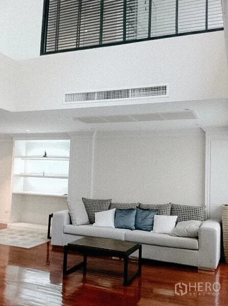 Townhouse for rent in Khlong Toei, Bangkok - Spacious living room with high ceiling and mezzanine-style window, sofa seating and built‑in shelves.