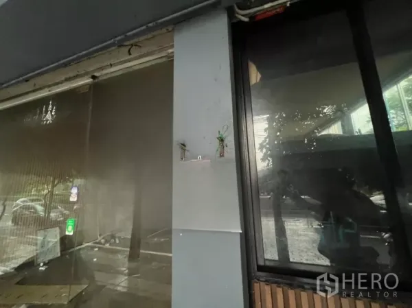 Shophouse for rent in Khlong Toei, Bangkok - Close-up of glass shopfront and column with mounting points and reflections, showing urban streetscape outside.