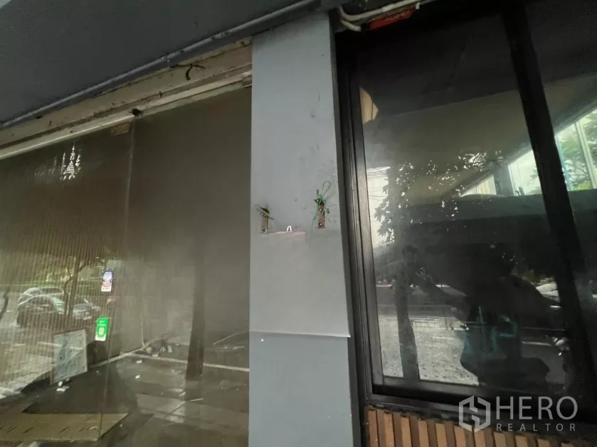 Shophouse for rent in Khlong Toei, Bangkok - Close-up of glass shopfront and column with mounting points and reflections, showing urban streetscape outside.