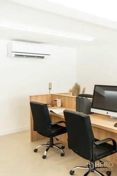 Office Space for rent in Khlong Toei, Bangkok - Close-up of two workstations with wooden partitions, computers, black chairs and a wall-mounted air conditioner.
