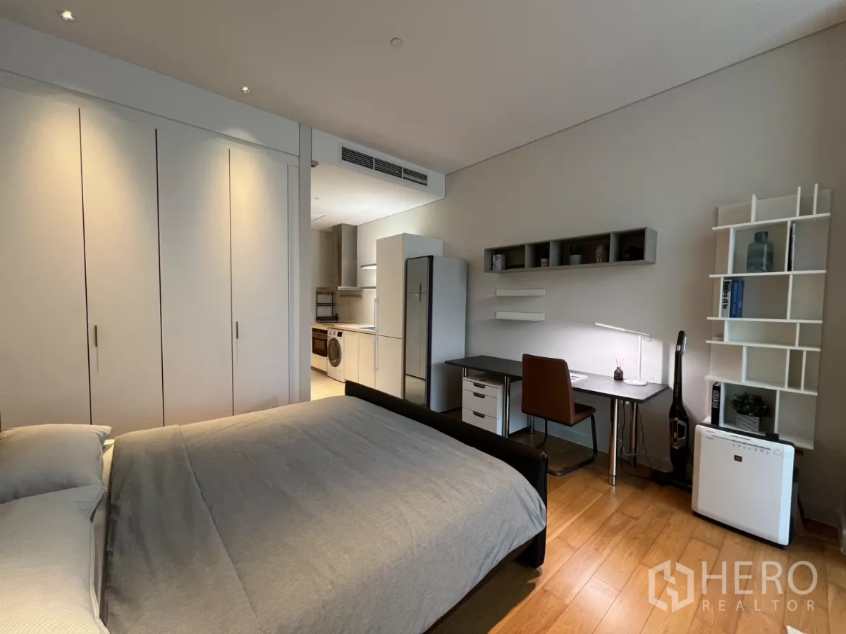 Condominium for rent in Pathum Wan, Bangkok - Bedroom area with large wardrobe and work desk, with compact kitchen visible in the background.
