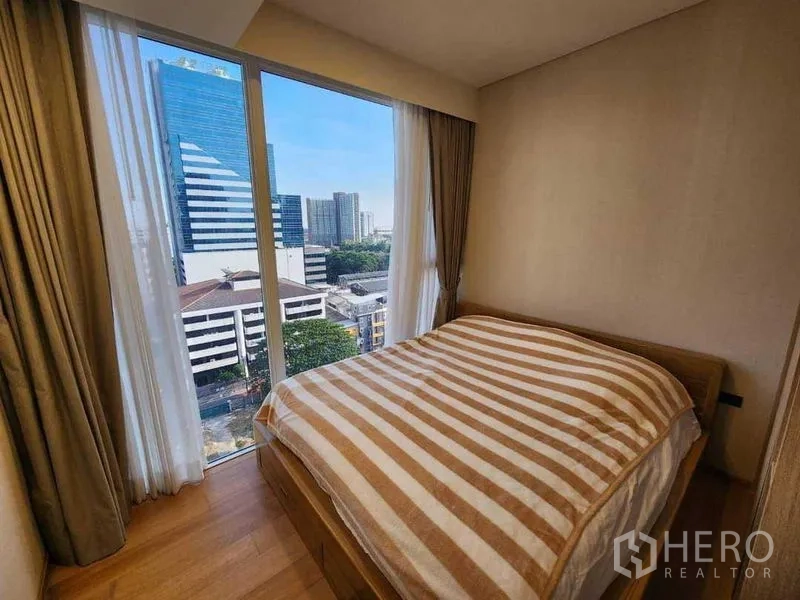 Condominium for rent in Khlong Toei, Bangkok - Cozy bedroom with striped bedding facing tall buildings and skyline.