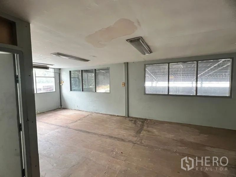 Warehouse for rent in Suan Luang, Bangkok - Empty office room inside the warehouse with windows, fluorescent lights, and wooden flooring panels.