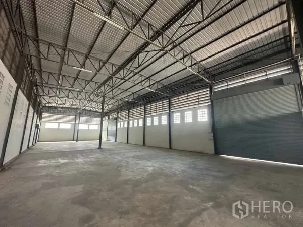 Warehouse for rent in Bang Bua Thong, Nonthaburi - Spacious warehouse interior with high steel-truss ceiling and roller shutter doors