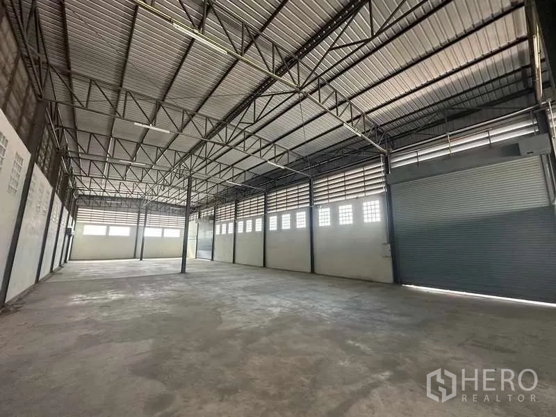 Warehouse for rent in Bang Bua Thong, Nonthaburi - Spacious warehouse interior with high steel-truss ceiling and roller shutter doors