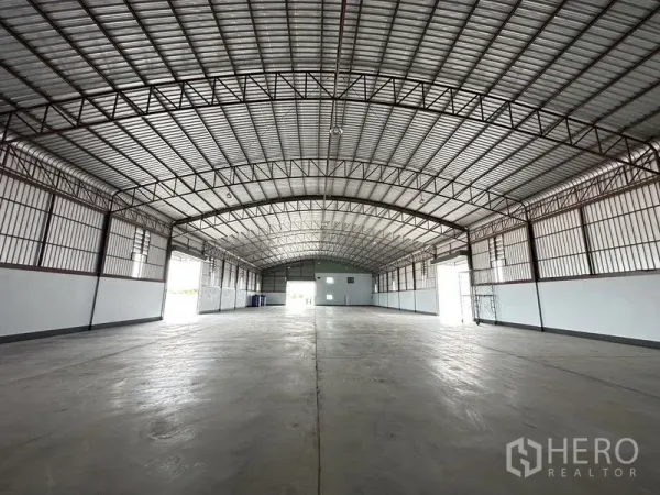Factory for rent or sale in Sai Noi, Nonthaburi - Central aisle perspective of the factory floor with multiple shutter doors and ample natural light.