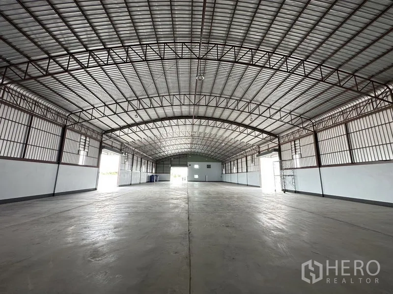 Factory for rent or sale in Sai Noi, Nonthaburi - Central aisle perspective of the factory floor with multiple shutter doors and ample natural light.