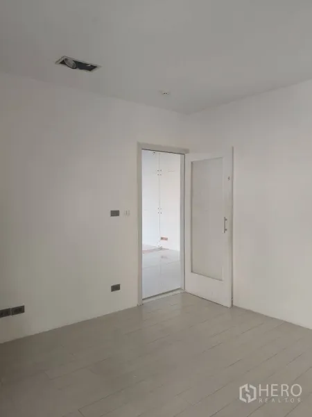 Office Space for rent in Khlong Toei, Bangkok - Minimal white room with light wood flooring and a glass door opening to the adjoining tiled office area.