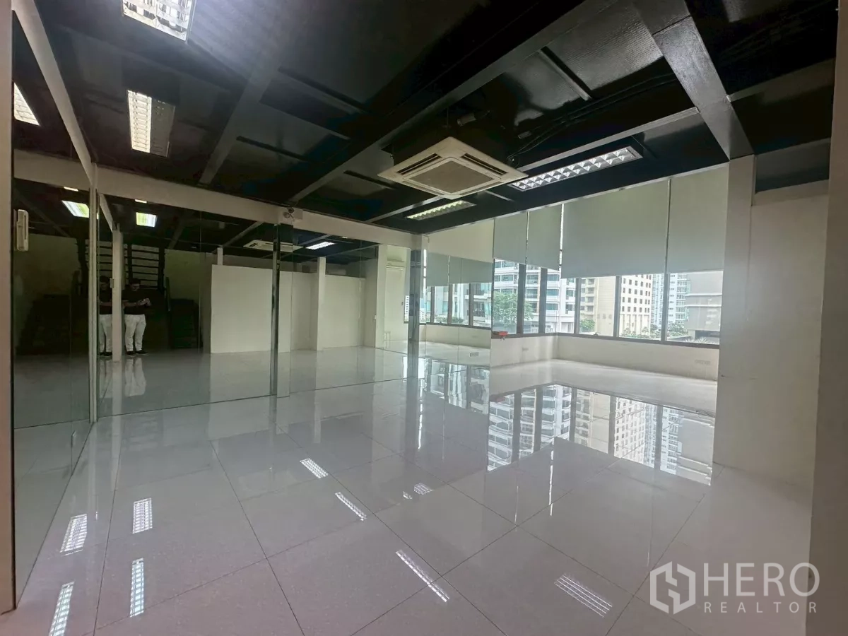 Office Space for rent in Khlong Toei, Bangkok - Open-plan office with mirrored wall, large windows and polished tiled floor.