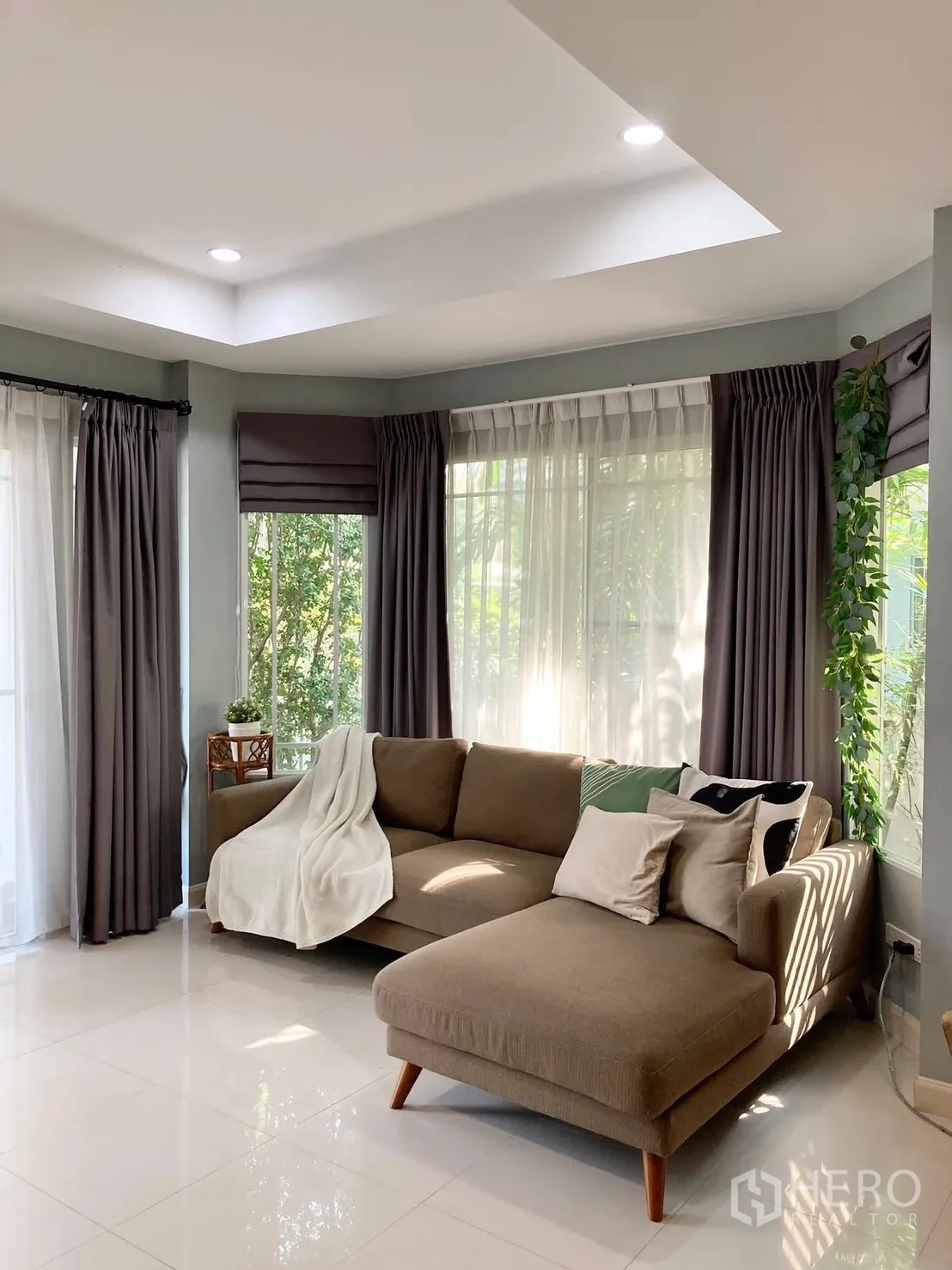 Detached House for rent in Prawet, Bangkok - Living room with L-shaped sofa, large windows and layered curtains.