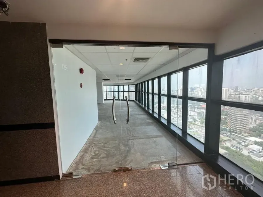 Office Space for rent - Glass double doors opening to a corridor lined with floor‑to‑ceiling windows and skyline views.