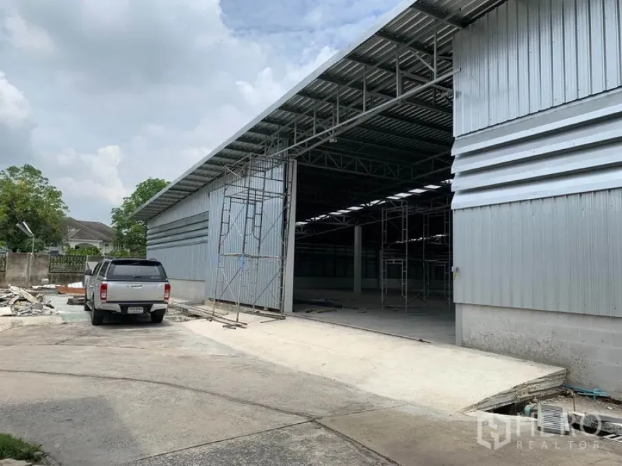 货栈 出租在Mueang Pathum Thani, Pathum Thani - 金属板外墙的仓库外观，超宽推拉门、高挑屋顶与混凝土装卸区，位于木昂巴吞他尼区。