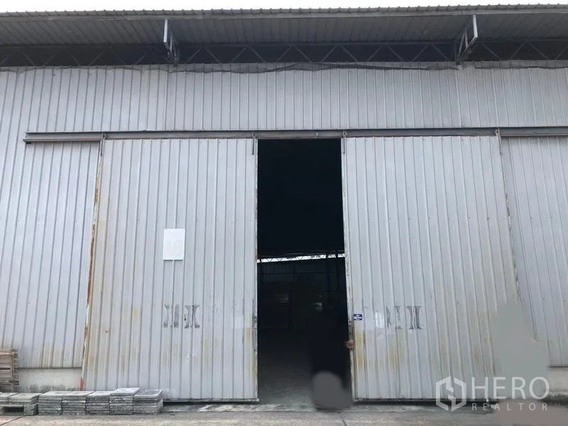 Warehouse for rent in Pak Kret, Nonthaburi - Front facade of the warehouse with a partially open sliding door and concrete apron.