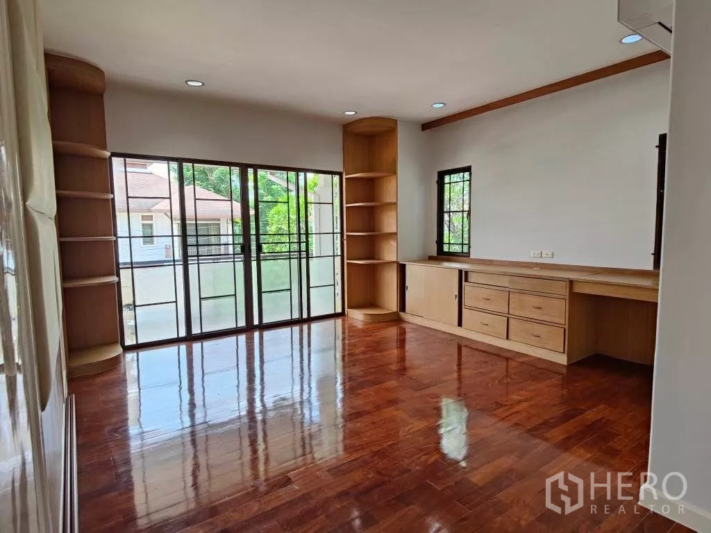 Detached House for rent or sale in Mueang Nonthaburi, Nonthaburi - Large bedroom with built-in shelves and desk, opening to balcony through sliding doors.