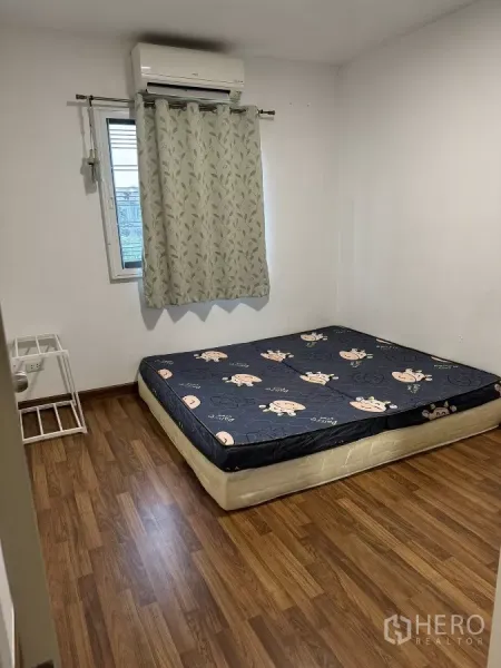 Townhouse for rent in Suan Luang, Bangkok - Simple bedroom with wood-look flooring, window with curtains, and wall-mounted air conditioner.