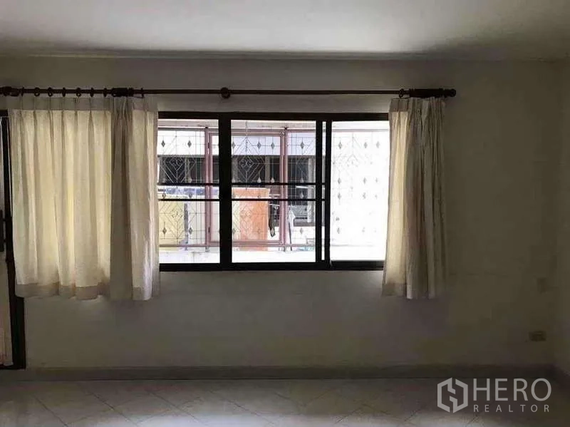 Townhouse for rent in Suan Luang, Bangkok - Upstairs bedroom with large window, curtains and natural light facing neighboring townhouses.
