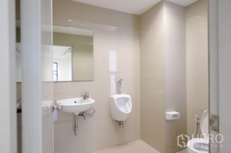 Office Space for rent in Chatuchak, Bangkok - Bright office restroom with sink, urinals and a large mirror on beige tiles.