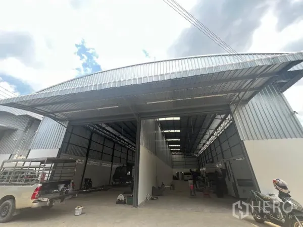 Warehouse for rent in Khlong Sam Wa, Bangkok - Angled exterior of a high-bay warehouse showing large roller-door entrances and metal roof canopy for truck loading.