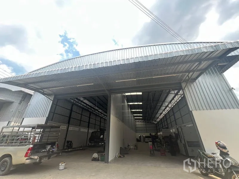 Warehouse for rent in Khlong Sam Wa, Bangkok - Angled exterior of a high-bay warehouse showing large roller-door entrances and metal roof canopy for truck loading.