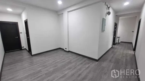 Townhouse for rent in Khlong Toei, Bangkok - Bright hallway with gray wood-look flooring and recessed lights inside the townhouse.