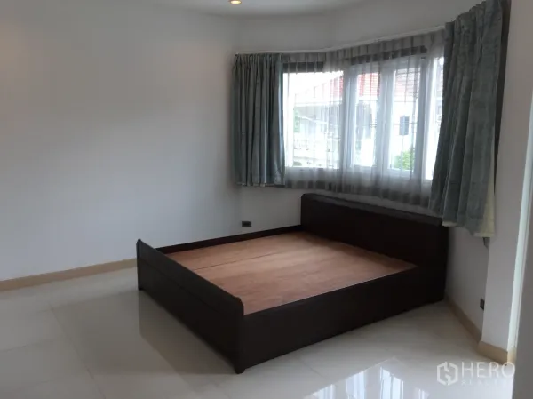 Townhouse for rent in Din Daeng, Bangkok - Bright bedroom with corner windows, sheer curtains and a dark wooden bed frame on glossy tile floors.